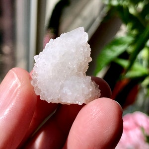 May include: A white crystal cluster with a heart-shaped form. The crystal is made up of many small, clear crystals.