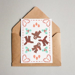 May include: A white card with a red, white, and blue gingerbread man design. The gingerbread men are in a circle with holly leaves and red berries around them. The card is in a brown envelope.