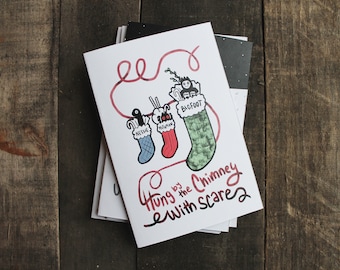 Puede incluir: Una tarjeta blanca con una cuerda roja y tres calcetines con diferentes personajes colgando de ella. Los calcetines son verdes, azules y rojos. El texto en la tarjeta dice "Hung by the Chimney with Scare".