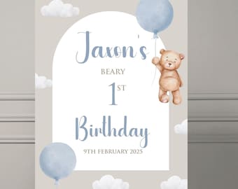 May include: A light brown teddy bear holding a blue balloon, with the text "Jaxon's Beary 1st Birthday 9th February 2025" on a beige background with white clouds.
