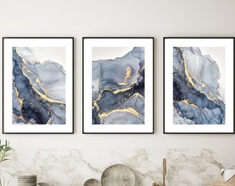 Puede incluir: Tres impresiones de arte abstracto enmarcadas con un diseño de mármol azul y dorado. Las impresiones están colgadas en una pared blanca sobre un gabinete gris con cajones.