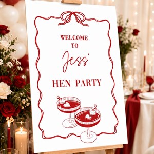 Puede incluir: Un letrero blanco sobre un caballete de madera con texto rojo y un borde decorativo. El letrero dice "Welcome to Jessi Hen Party" con ilustraciones de c&oacute;cteles. El fondo incluye globos, flores y velas.