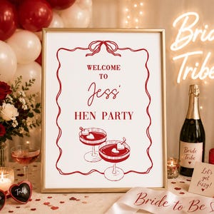 Puede incluir: Un letrero enmarcado con el texto "WELCOME TO Jessi HEN PARTY" en rojo, con ilustraciones de c&oacute;cteles. La escena incluye globos, flores, champ&aacute;n, velas y un letrero de ne&oacute;n "Bride Tribe", creando un ambiente festivo.