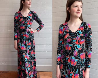May include: A long-sleeved maxi dress with a black background and a colorful floral print. The dress has a scoop neck and long sleeves. The flowers are in shades of pink, red, blue, and turquoise.