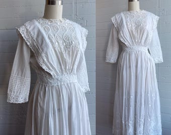 May include: A white cotton dress with a lace overlay and a gathered skirt. The dress has a round neckline and 3/4 sleeves.