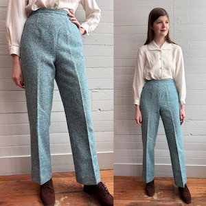 May include: High-waisted, teal-colored herringbone pants. The pants have a tailored fit with a straight leg. The fabric has a textured appearance. The pants are paired with a cream-colored blouse and brown shoes.