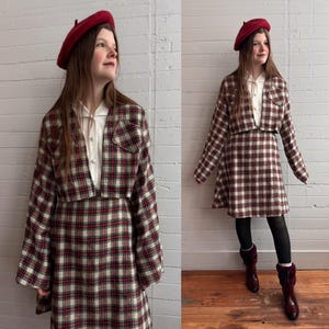 Puede incluir: Traje de falda vintage a cuadros rojos, crema y verdes. El conjunto incluye una chaqueta y una falda a juego, usado con una boina roja y una camisa blanca con cuello. La falda llega a la rodilla. Estilo retro clásico.