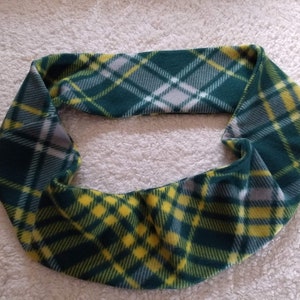 May include: A green, yellow, and white plaid infinity scarf made of soft fleece material. The scarf is a continuous loop, designed to be worn around the neck. The plaid pattern features a repeating grid design.