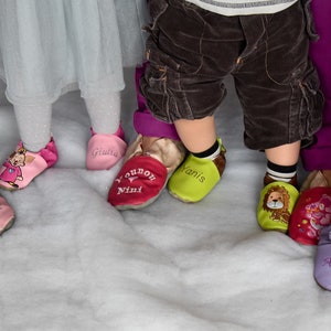 Peut inclure: Un groupe d'enfants portant des chaussures souples à semelles souples personnalisées. Les chaussures sont roses, rouges, vertes et violettes avec des noms et des motifs brodés.
