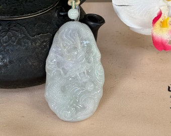 May include: A light green jade pendant carved with a detailed dragon design. The pendant is hanging from a string with a small bead.
