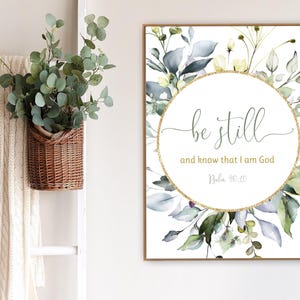 Puede incluir: Una impresión de acuarela con un círculo de purpurina dorada y el texto "be still and know that I am God, Psalm 46:10". El fondo es un lienzo blanco con un diseño floral en tonos verdes y azules.