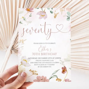 May include: A rectangular birthday invitation card featuring a floral design with pink, white, and gold botanical illustrations. The text reads: seventy, Esther's 70TH BIRTHDAY, SATURDAY, DECEMBER 12TH AT 2:00PM, TWELVE COUNTRY CLUB, 1200 FOREST RD, LOS ANGELES, CA 07854, RSVP TO JENN AT 7771234567 BY DECEMBER 5TH.