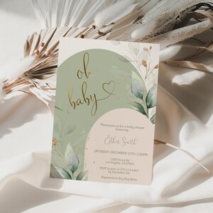 Op de afbeelding: Een rechthoekige uitnodigingskaart voor een babyshower met een saliegroene boog, een beige halve cirkel en aquarel eucalyptusbladeren. De tekst luidt oh baby in gouden cursief met een hartje, gevolgd door de evenementdetails voor Esther Smith.