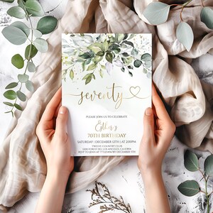 May include: A rectangular invitation card for a 70th birthday celebration featuring a watercolor botanical design with green leaves and gold accents. The text reads: seventy, please join us to celebrate Esther's 70th birthday, Saturday, December 12th, at 2:00pm, Twelve Country Club, 1200 Forest Rd. Los Angeles, CA 07854, RSVP to Jenn at 7771234567 by December 5th.