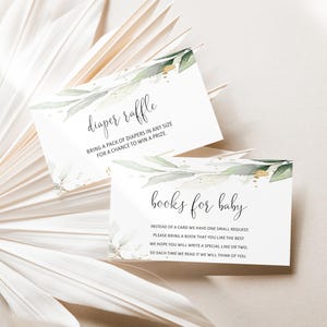 May include: Two white baby shower cards with elegant script, one reading "diaper raffle" and the other "books for baby." Both cards feature watercolor greenery and gold accents. The cards are set against a neutral, textured background.