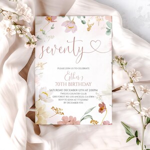 May include: A rectangular birthday invitation card featuring a floral design with pink, yellow, and green watercolor flowers. The text reads: seventy, PLEASE JOIN US TO CELEBRATE, Esther's 70TH BIRTHDAY, SATURDAY, DECEMBER 12TH AT 2:00PM, TWELVE COUNTRY CLUB, 1200 FOREST RD. LOS ANGELES, CA 07854, RSVP TO JENN AT 777.123.4567 BY DECEMBER 5TH.