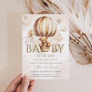 May include: A gender reveal invitation card with a watercolor hot air balloon design. The card features a teddy bear in the balloon basket and the text "Oh Baby, He or She?" The invitation is for Esther and David's gender reveal.