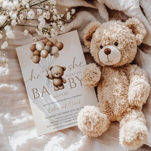 May include: A gender reveal invitation with a teddy bear illustration holding balloons. The invitation reads "He or She, What Will Baby Be?" and includes event details. A plush teddy bear sits beside the invitation on a soft, neutral-toned surface.