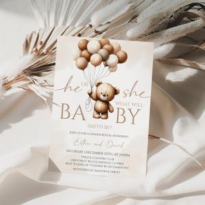May include: A gender reveal invitation card with a teddy bear holding balloons. The text reads "He or She, What Will Baby Be?" in brown script. The invitation includes event details and is set against a neutral background.