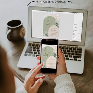 Op de afbeelding: Een digitale uitnodigingssjabloon voor een babyshower weergegeven op een laptopscherm en een smartphone. Het ontwerp bevat saliegroene en zachtroze bogen, botanische bladillustraties en de tekst 'oh baby' in een scriptlettertype met details.