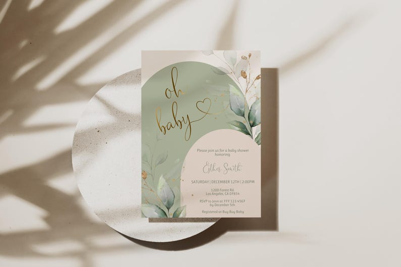 Op de afbeelding: Een rechthoekige uitnodigingskaart voor een babyshower met een saliegroen boogontwerp, goudfolie tekst oh baby en botanische aquarelillustraties. De kaart bevat gedrukte evenementdetails voor Esther Smith op een lichtbeige achtergrond.