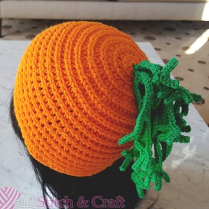 Puede incluir: Sombrero de ganchillo naranja y verde con forma de zanahoria. El sombrero tiene una parte superior de ganchillo verde que se asemeja a la parte superior frondosa de una zanahoria.