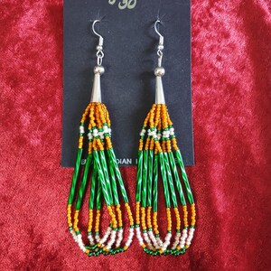 May include: A pair of long, beaded earrings with green, orange, and white beads. The earrings are hanging from silver hooks.