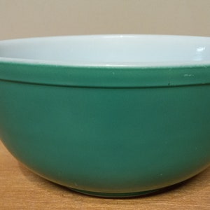 May include: A teal mixing bowl with a white interior. The bowl has a rounded shape and a smooth, glossy finish. The interior is a bright white, contrasting with the exterior's solid teal colour. A classic kitchenware item.