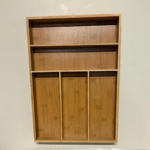 May include: A rectangular bamboo cutlery organizer tray featuring a light brown wood grain finish. The tray is divided into one horizontal top compartment and three vertical bottom compartments, providing organized storage sections for kitchen utensils.