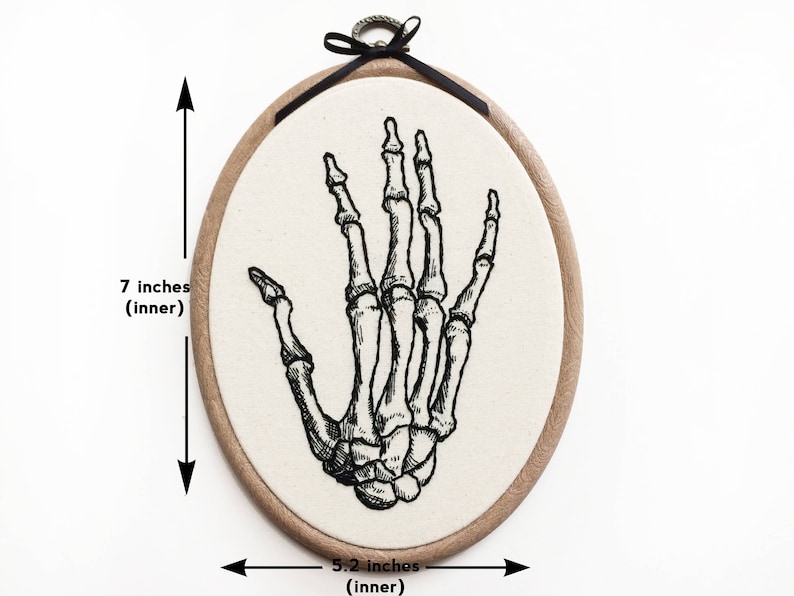 An oval embroidery hoop. A detailed embroidery of the bones of the hand is on the ivory fabric.