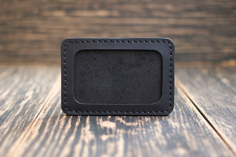 May include: A black leather card holder with a stitched border and a blank window for displaying identification.