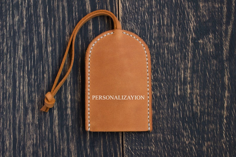 Op de afbeelding: Een bruine leren sleutelhanger met een witte gestikte rand en het woord "PERSONALISATIE" in wit gegraveerd.