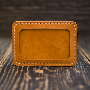 May include: A brown leather card holder with a stitched border and a blank rectangular space in the center.