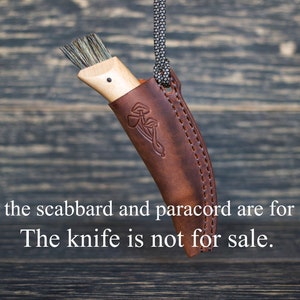 K&ouml;nnte beinhalten: Ein braunes Lederscheide mit einer Paracordschlaufe, die daran h&auml;ngt. Die Scheide hat ein gepr&auml;gtes Pilzdesign. Das Messer in der Scheide steht nicht zum Verkauf. Nur die Scheide und das Paracord sind zum Verkauf.