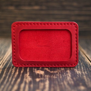May include: A red leather ID card holder with a stitched border. The holder is empty and ready for personalization.