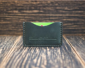 May include: A dark green leather card holder with a stitched edge and the text "Leather Handmade" in a circle with a globe icon.