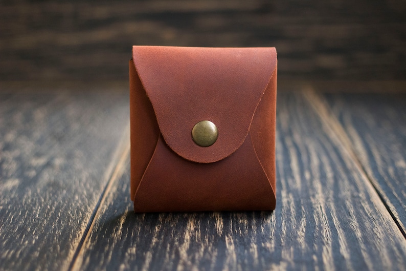Pode incluir: Uma pequena bolsa de moedas de couro marrom com fecho de bot&atilde;o de metal.
