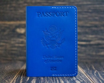 Könnte beinhalten: Ein blaues Leder-Reisepass-Etui mit den Worten "PASSPORT", "United States of America" und dem Siegel der Vereinigten Staaten.