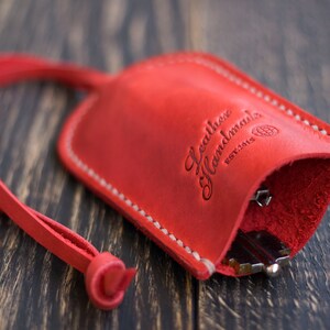 May include: Red leather key holder with a white stitch detail and a strap. The holder has the text "Leather Handmade Est. 2015" embossed on the front.