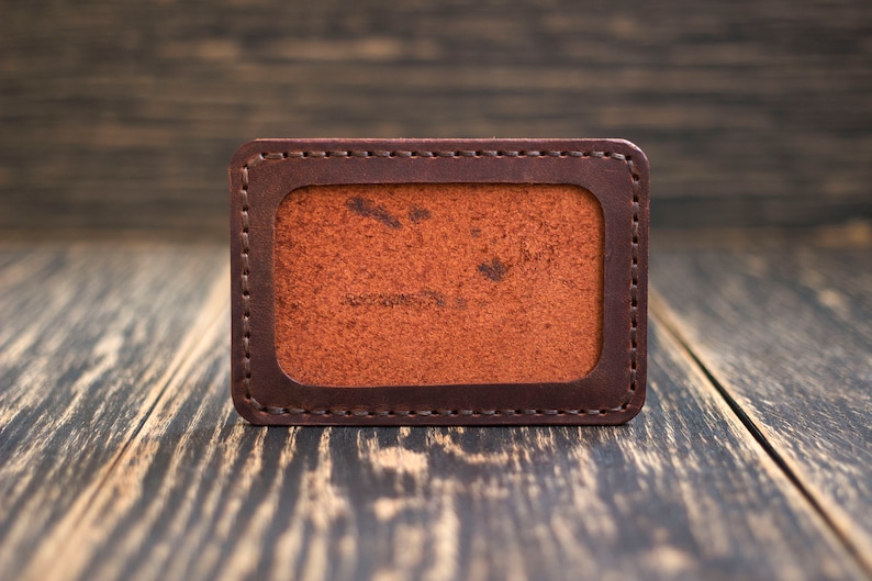 May include: A brown leather card holder with a stitched border and a blank interior.