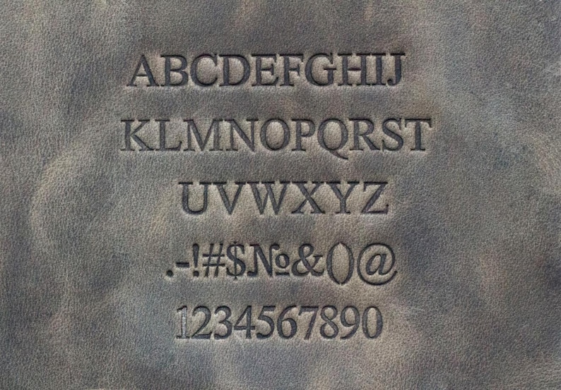Op de afbeelding: Een close-up van een bruin lederen oppervlak met een gestempeld alfabet en cijfers. De letters zijn in hoofdletters en de cijfers zijn in een standaard lettertype.