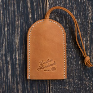 May include: A brown leather key chain with a stitched edge and a loop. The keychain has the text "Leather Handmade" and a globe symbol.