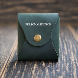 Pode incluir: Uma bolsa de couro verde escura estilo envelope com fecho de bot&atilde;o de lat&atilde;o. A bolsa tem a palavra "PERSONALIZA&Ccedil;&Atilde;O" gravada na frente.