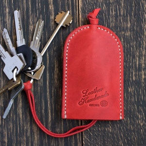 May include: Red leather key holder with a white stitch detail and the text "Leather Handmade EST.2013" in white. The key holder is attached to a red cord.