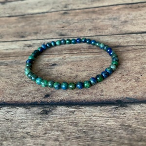 May include: A blue and green gemstone beaded bracelet. The bracelet is made of small, round beads that are strung together on a thin cord.