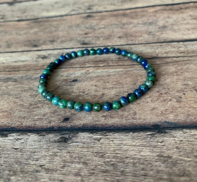 May include: A blue and green gemstone beaded bracelet. The bracelet is made of small, round beads that are strung together on a thin cord.