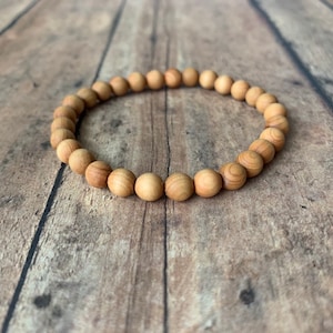 May include: A wooden bead bracelet with natural brown tones. The bracelet is made of round beads and is lying on a wooden surface.