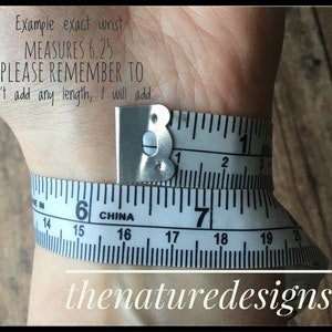 May include: A white measuring tape wrapped around a wrist, showing a measurement of 6.25 inches. The text "Example exact wrist MEASURES 6.25 PLEASE REMEMBER TO Don't add any length, I will add." is visible above the tape.