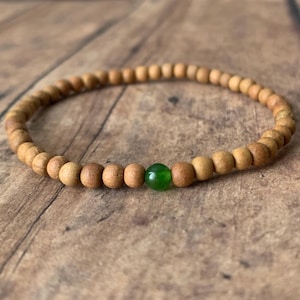 May include: A wooden beaded bracelet with a single green bead. The bracelet is made of natural wood and has a simple, elegant design.
