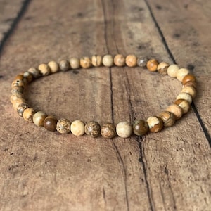 May include: A brown and white beaded bracelet with a natural stone look. The bracelet is made of small, round beads that are strung together on a thin cord.